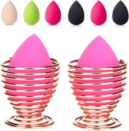 Pair of rose gold metal spiral stands for drying and storing makeup sponges, shown on a dresser.