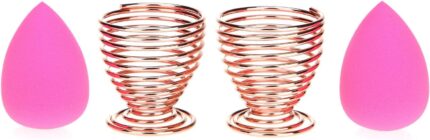 Pair of rose gold metal spiral stands for drying and storing makeup sponges, shown on a dresser.