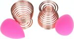 Pair of rose gold metal spiral stands for drying and storing makeup sponges, shown on a dresser.