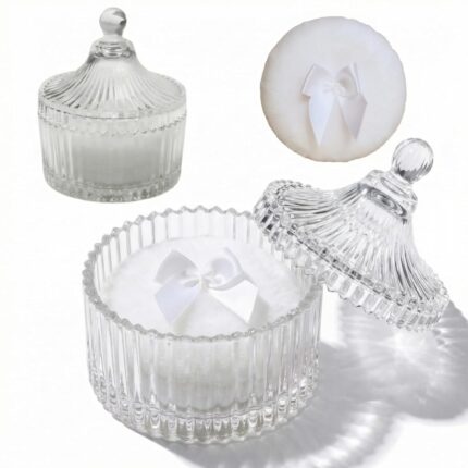 Two white velour body powder puffs with bows inside a clear crystal glass container on a white background