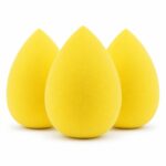 Three yellow teardrop-shaped makeup sponge blenders on a clean surface, ready for foundation application.